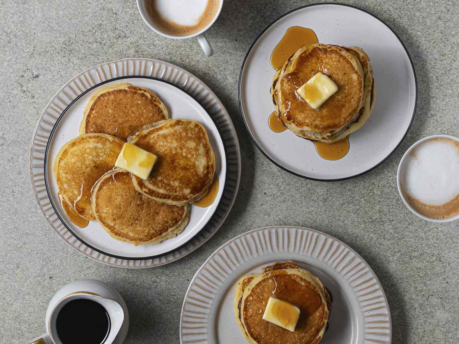 Plates of pancakes with butter and syrup on a stone counter.