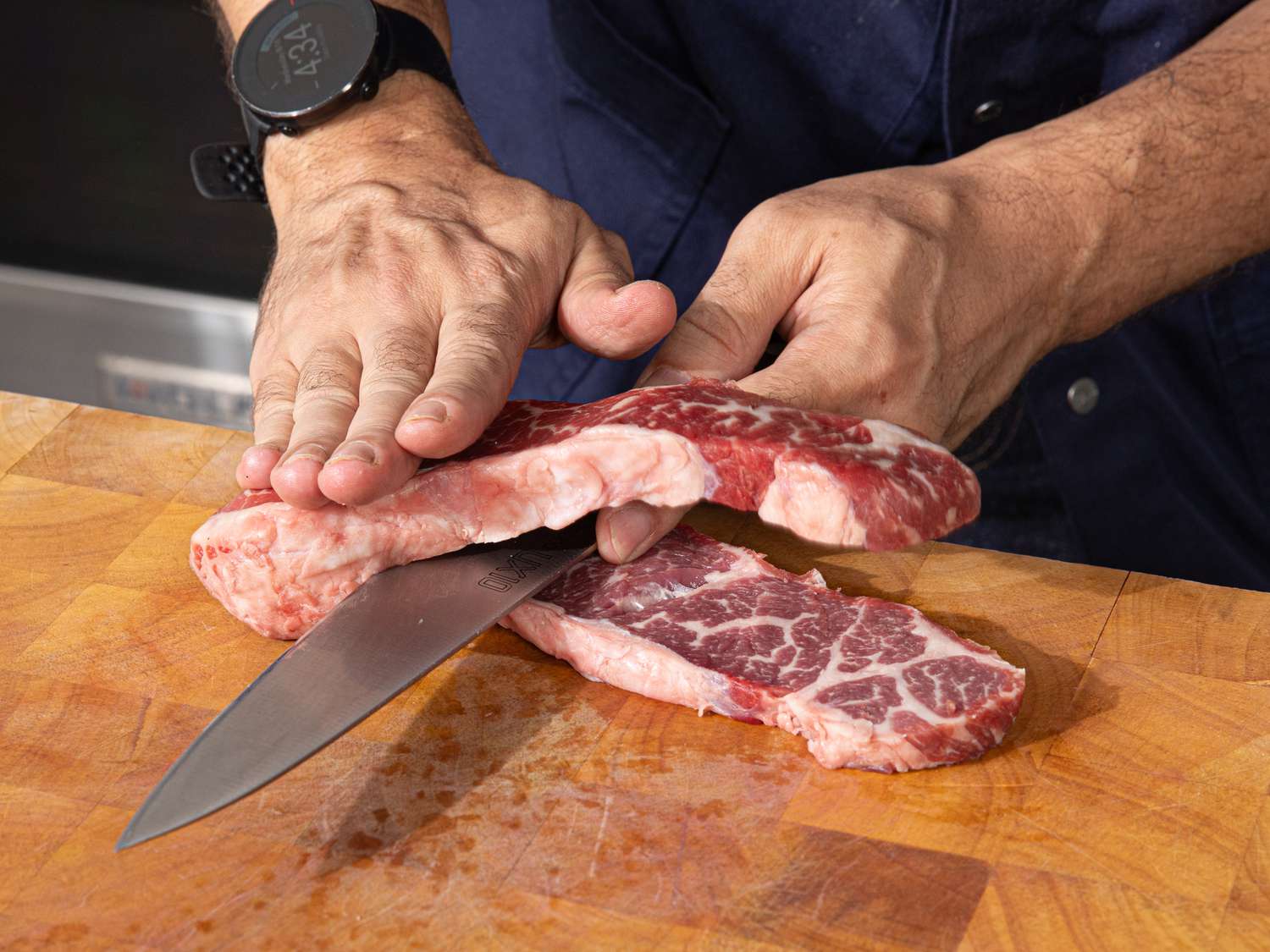 A raw boneless beef short rib being sliced horizontally through the middle to butterfly it.