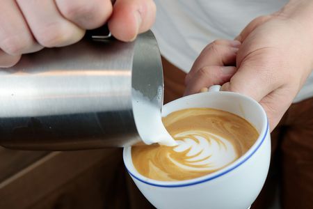 hands holding a milk pitcher latte cup pouring latte art onto the surface